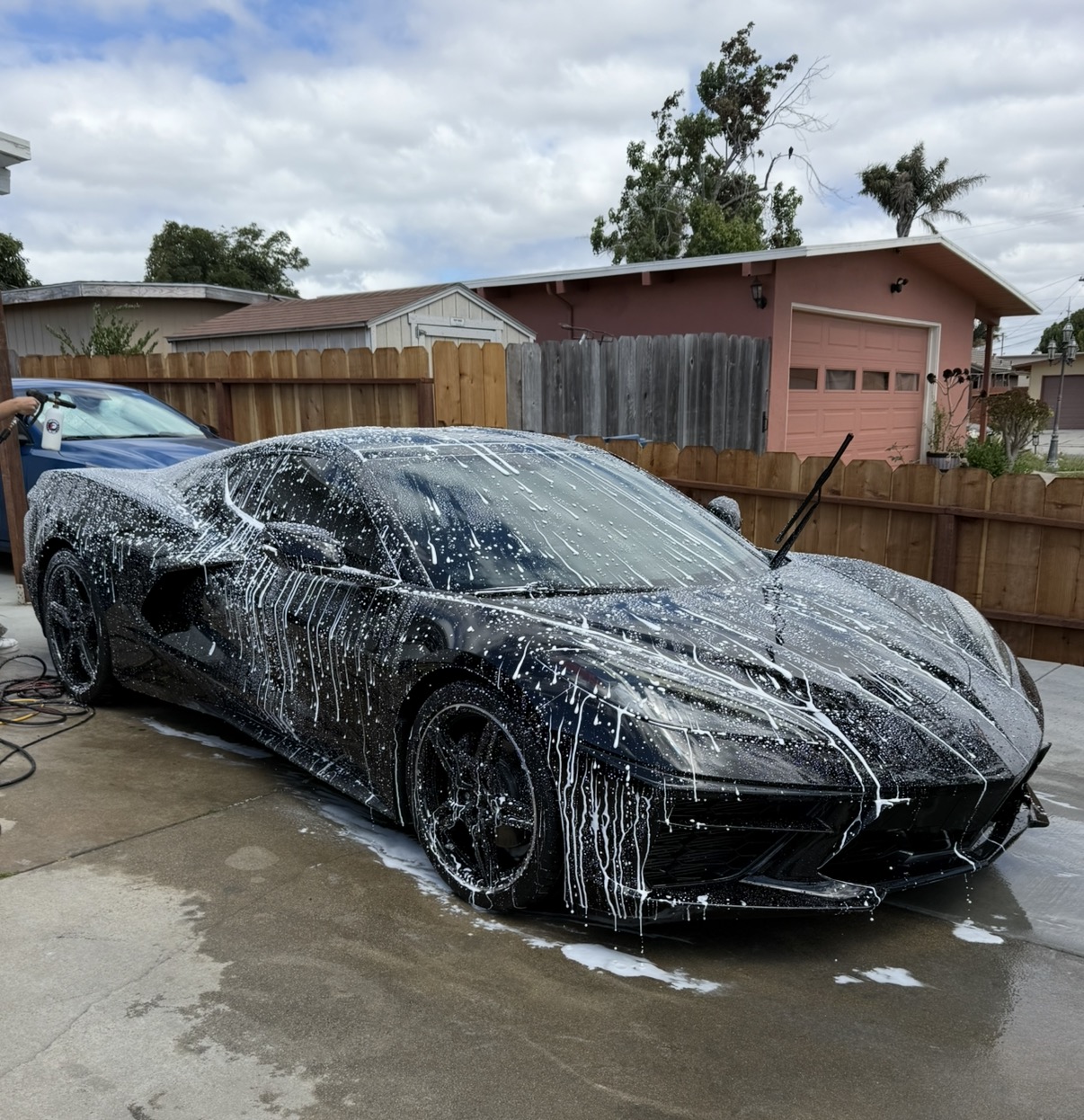 Black Chevrolet Corvette covered in thick wash foam during pre-coating decontamination in Monterey, CA